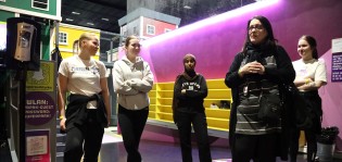 Opettaja ja viisi opiskelijaa poseeraavat kameralle Superparkin sisääntulon luona. Taustalla näkyy pinkkejä ja keltaisia taustaseiniä.